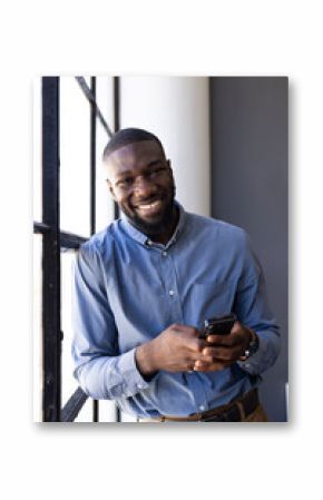 Smiling businessman holding smartphone, standing by window in office setting