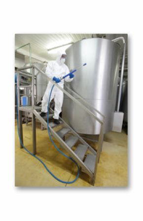 worker in white protective uniform with  high pressure washer on stairs at large industrial process tank preparing to cleaning