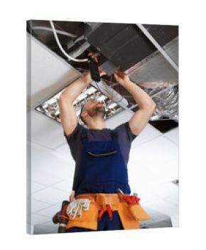 Male technician measuring voltage during repair of industrial air conditioner indoors
