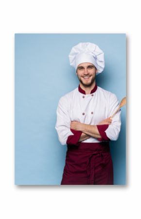 Portrait of positive toothy chef cook in beret, white outfit having tools in crossed arms looking at camera.