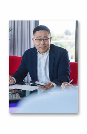 Businessman discussing strategy in office meeting, holding smartphone and papers