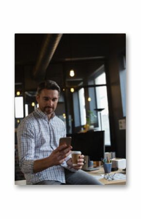 Businessman holding coffee and smartphone, checking messages in modern office, copy space