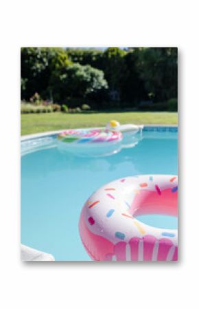 Pink sprinkled donut float is drifting on clear pool water near unicorn float in sunny backyard