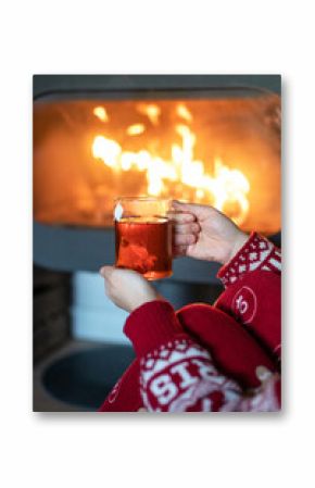 Side view of unrecognizable female in red warm sweater sitting with cup of tea near chimney and enjoying cozy Christmas night