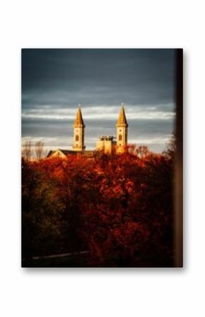 Vertical shot of church towers behind autumn-colored trees