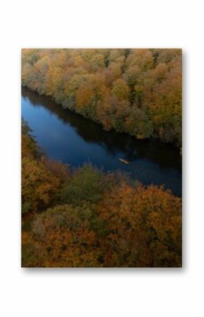 Aerial of a small kayak in the calm river surrounded by the yellow autumn forest