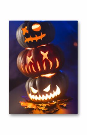 Vertical image of three illuminating carved pumpkins tower on blue background