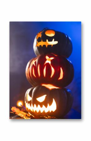 Vertical image of three illuminating carved pumpkins tower on blue background