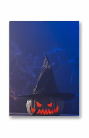 Vertical image of carved pumpkin wearing witch hat with copy space on blue background