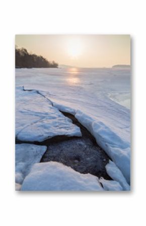 Rock under cracked ice at a frozen lake in Finland in the spring at dawn.