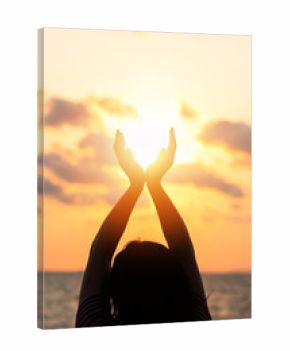 June summer sun solstice concept and silhouette of happy young woman’s hands relaxing, meditating and holding sunset against warm golden hour sky on the beach with ocean or sea background