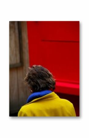 Vertical shot of a short-haired woman standing on the street in front of a red wall