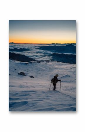 Traveler with trekking poles on snowy mountain slope