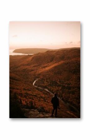 Aerial view of a person standing on a cliff, enjoying view of river in mountains in autumn at sunset