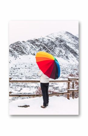 Side view of anonymous person standing under colorful umbrella and enjoying amazing view of Pyrenees mountain ridge covered with snow in winter