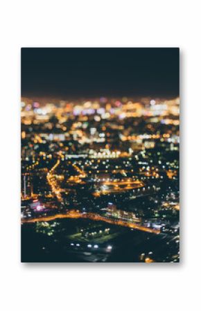 True tilt shift shooting of highway in residential district during night in metropolis from high point: multiple residential houses, road in focus in foreground, strong bokeh in background