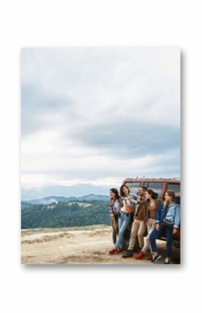 Pleasant happy young friends standing near their car while enjoying view from the mountain hill