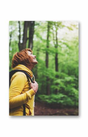 smiling tourist traveler with backpack into road at summer green forest, girl hiker in yellow hoody looking and enjoying the breath of fresh air in trip, relax holiday concept, blurred background