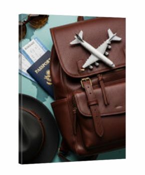 Brown leather backpack with airplane model, passport, boarding pass, sunglasses and hat on world map background, symbolizing travel and adventure