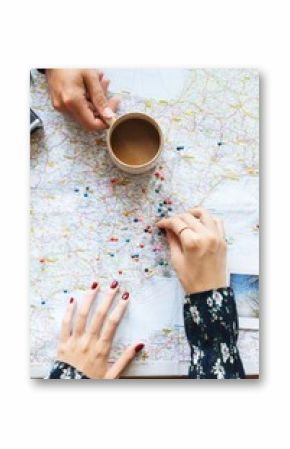 Hands on a map with colorful pins, planning a journey. Map and pins show travel ideas. Coffee cup nearby. Map, pins, and travel planning scene. Women planning a trip on a map.