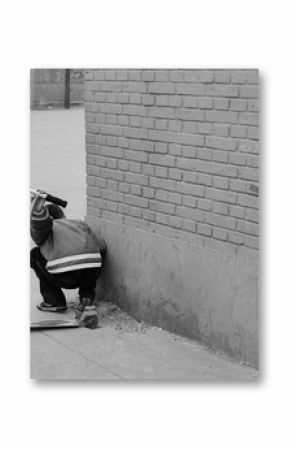 A boy with a scooter peers around a corner at his friends in Beijing, China