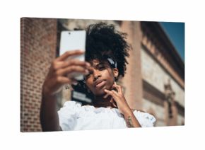 Trendy black woman taking selfie outdoors