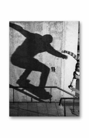 Dynamic black-and-white photograph capturing a skateboarder in mid-action with a dramatic shadow against a textured wall, showcasing skill and urban skateboarding culture in an outdoor urban setting.
