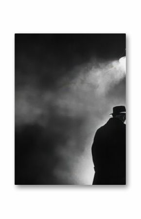Man in coat and hat stands under a street lamp in a foggy and dark black and white outdoor scene