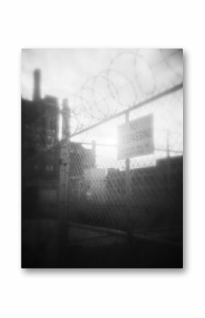 Old fashioned black and white image of a barbed wire fence in front of an old factory building
