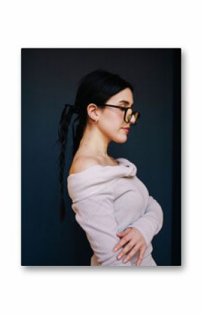 Stylish woman in white dress with glasses posing indoors against a yellow background