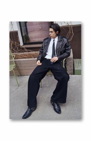 Man in leather jacket sitting on green chair outdoors  