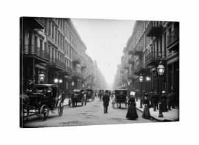 A historic black and white photo of a busy street with horse drawn carriages and people in vintage clothing