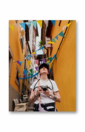 A tourist in a white shirt and black cap stands in a narrow alley