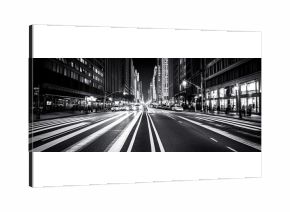 High-contrast black and white photo of a city street illuminated by artificial lights, sharp shadows, moody ambiance