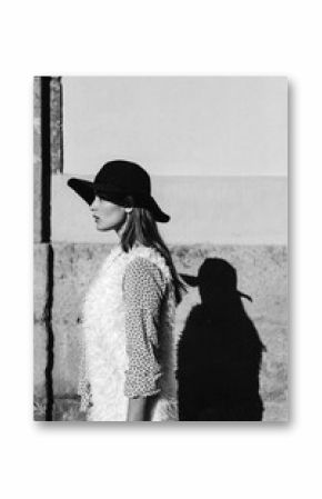 Stylish woman in black hat casting shadow on wall