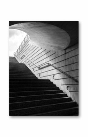 A captivating black and white photograph features an upward leading staircase within a curved architectural structure, evoking a sense of mystery and elegance.