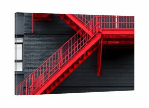 A bright red fire escape ladder on a black and white city building
