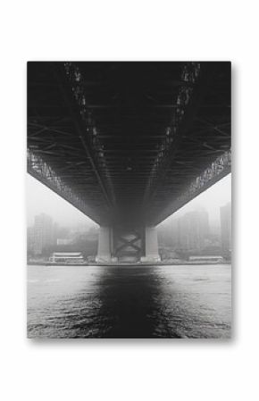 A monochrome view of a bridge above a foggy cityscape.