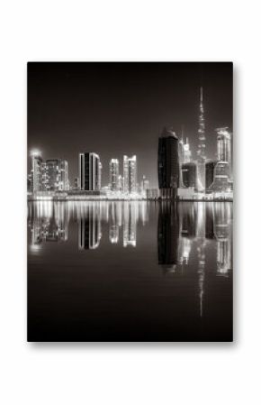 Urban city skyline with illuminated skyscrapers and waterfront railing in black and white at night, Dubai Marina bay UAE