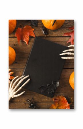 Vertical image of halloween decorations, skeleton hands on notebook, copy space on brown background