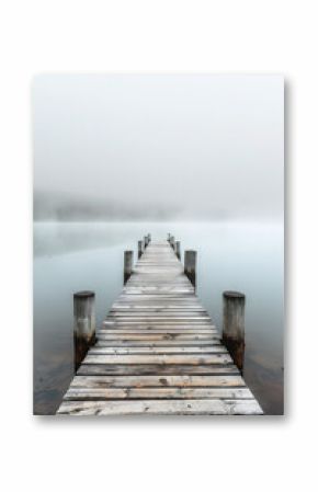 A foggy day at a pier with a wooden bridge. The water is calm and the sky is overcast