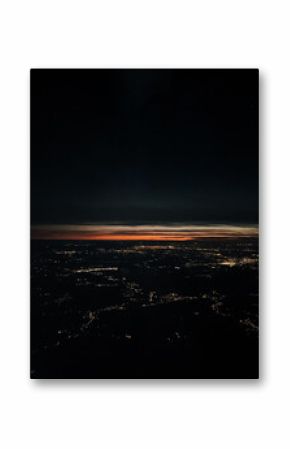 View from the airplane window of the city at night and the late sunset. Aerial view of illuminated city from plane