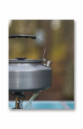 A kettle is heating up on a small camping stove as steam begins to rise in the cool forest air