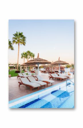 Relaxing afternoon by the swimming pool of a luxury resort with palm trees and cabanas at sunset
