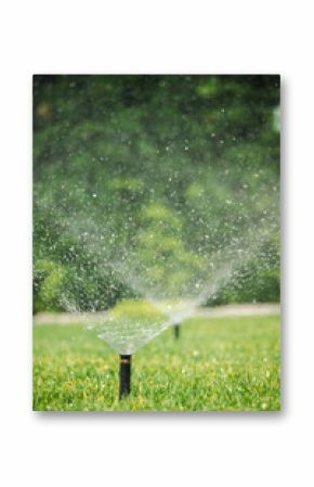 Closeup of automatic lawn sprinklers in action, spraying water over green grass during a sunny day in a landscaped garden