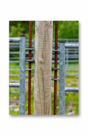 Close-up of rusty gate hinges connecting to a wooden post in a green rural setting, showcasing weathered materials and nature.