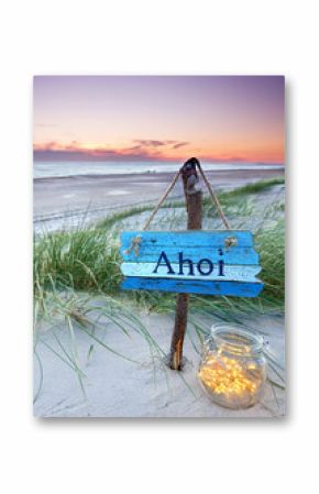 weathered sign with AHOI text in the dunes in sunset sky