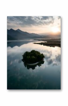 A serene image captures a small, green island nestled in the center of a calm lake, with its reflection mirrored perfectly in the still water