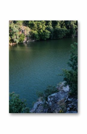 A serene river, framed by dense green trees and rocky cliffs, flows peacefully under a summer sky.
