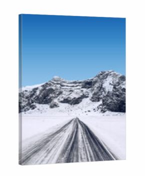 View of a long road stretches towards the snow-covered mountain under a bright blue sky on a winter day. Beautiful landscape for a natural or winter background or wallpaper
